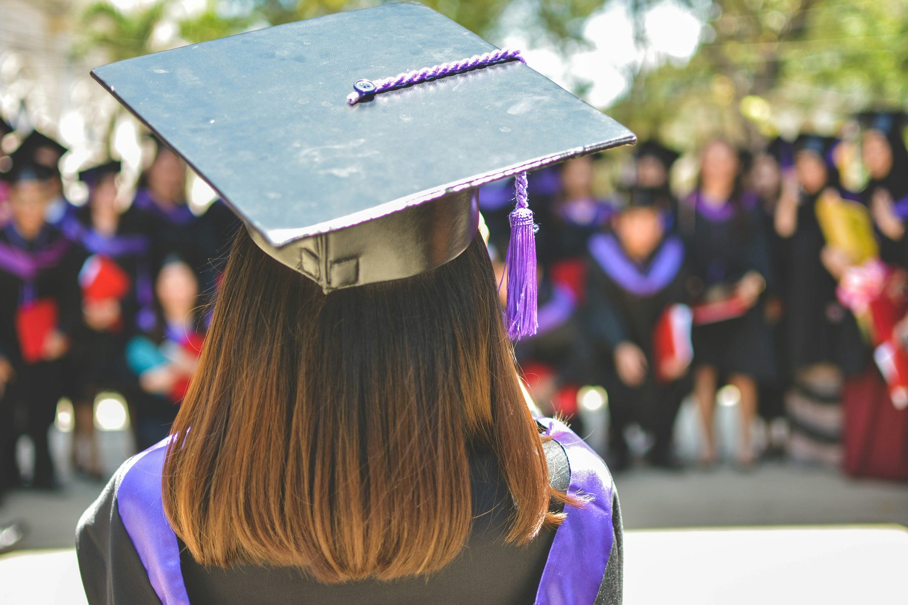 Graduate at commencement with cohort of peers in background